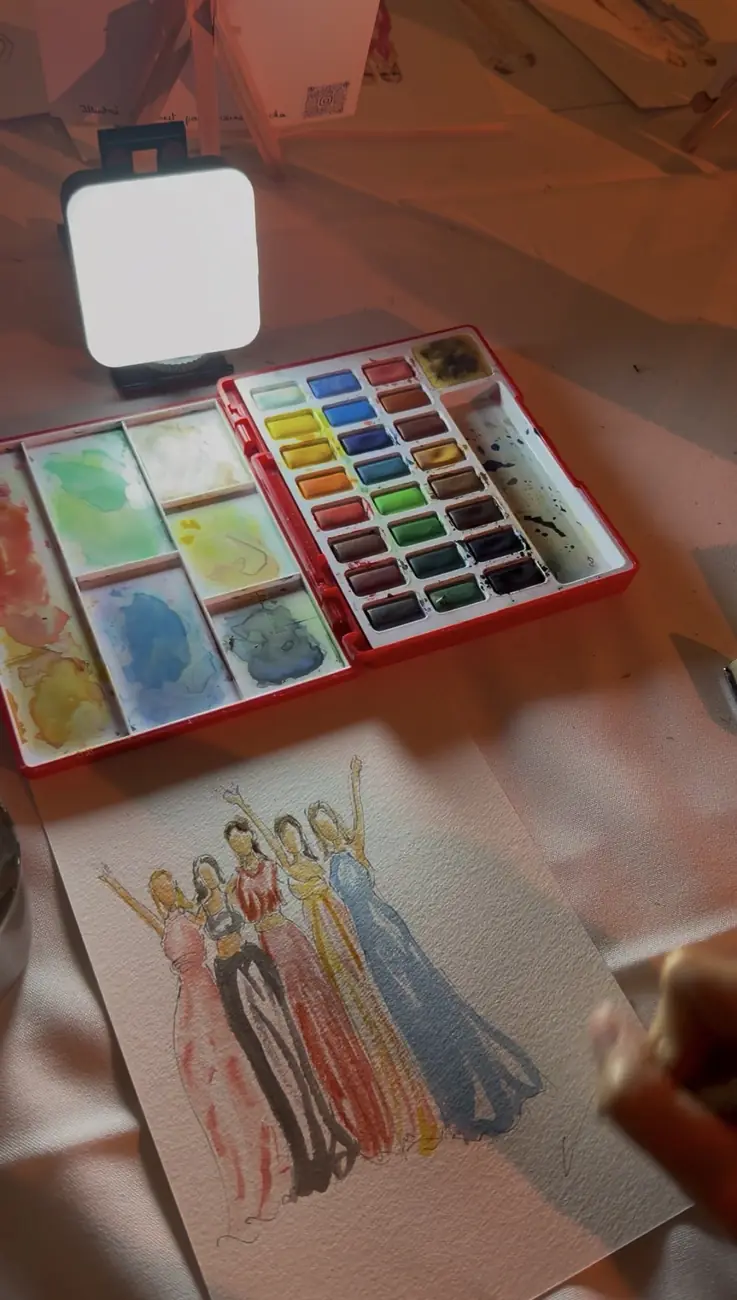 Silhouette aquarelle d'un groupe d'invitées en robes longues, à côté de la palette et de la lampe de l'illustratrice