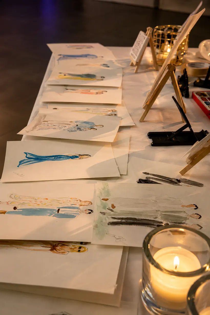Illustrations de mode à l'aquarelle étalées sur la table de l'illustratrice, à la lueur des bougies