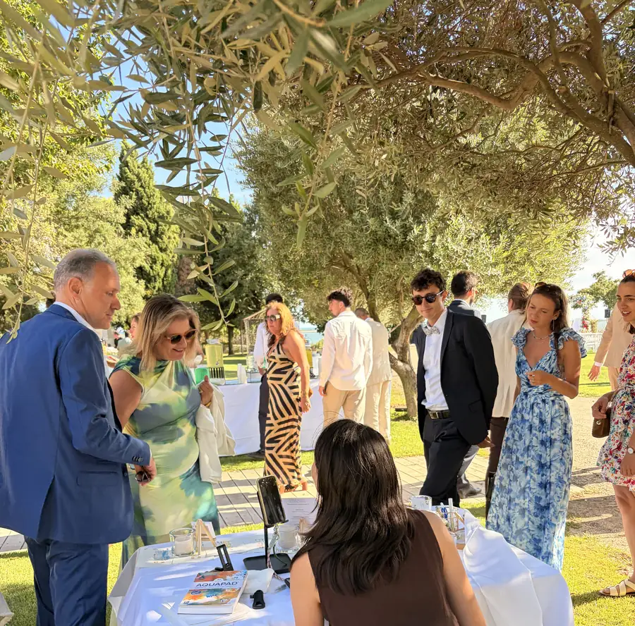 Invités découvrant le poste de l'illustratrice live sous les oliviers, pendant le cocktail au Domaine des Moures