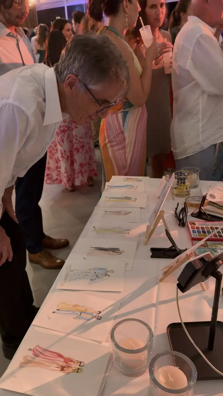 Invité découvrant les silhouettes de mode réalisées en direct, exposées sur la table de l'illustratrice