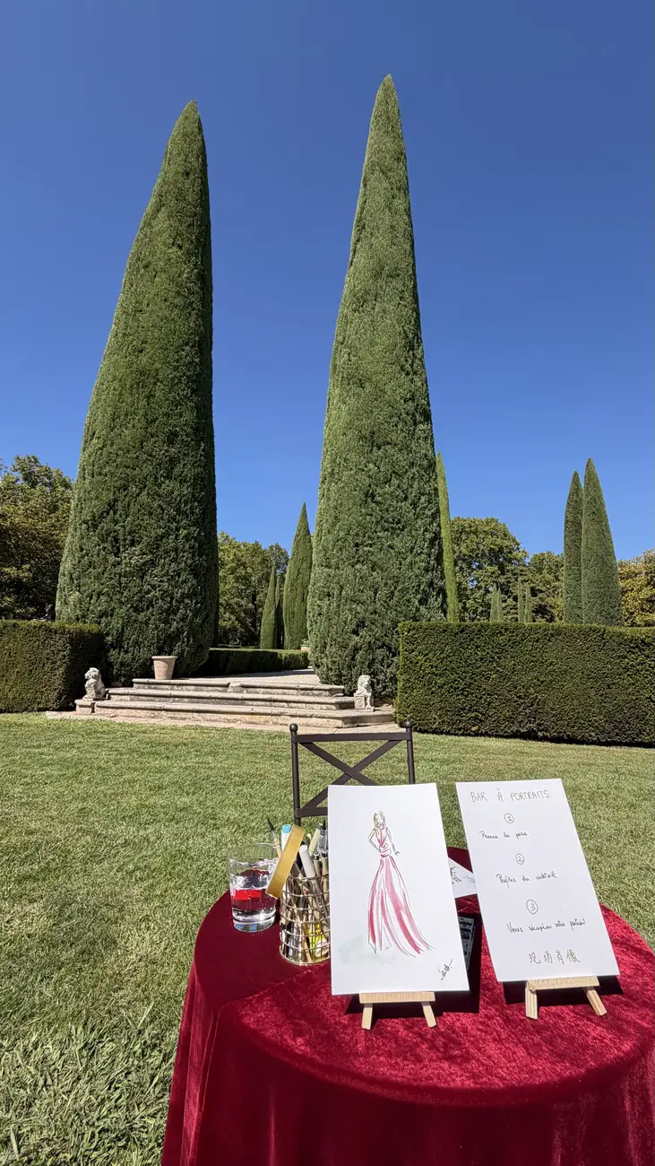 Table de l'illustratrice live nappée de velours rouge, chevalets et menu, devant les cyprès du Château de Sannes